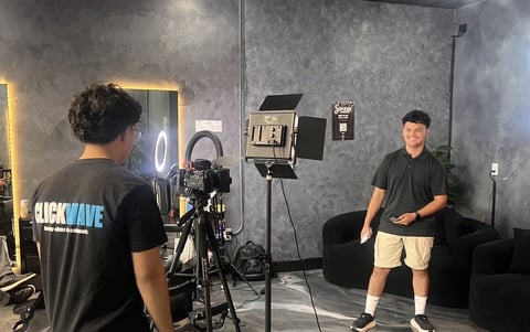 Two people in a professional video studio with cameras, lighting equipment, and grey walls during a filming session