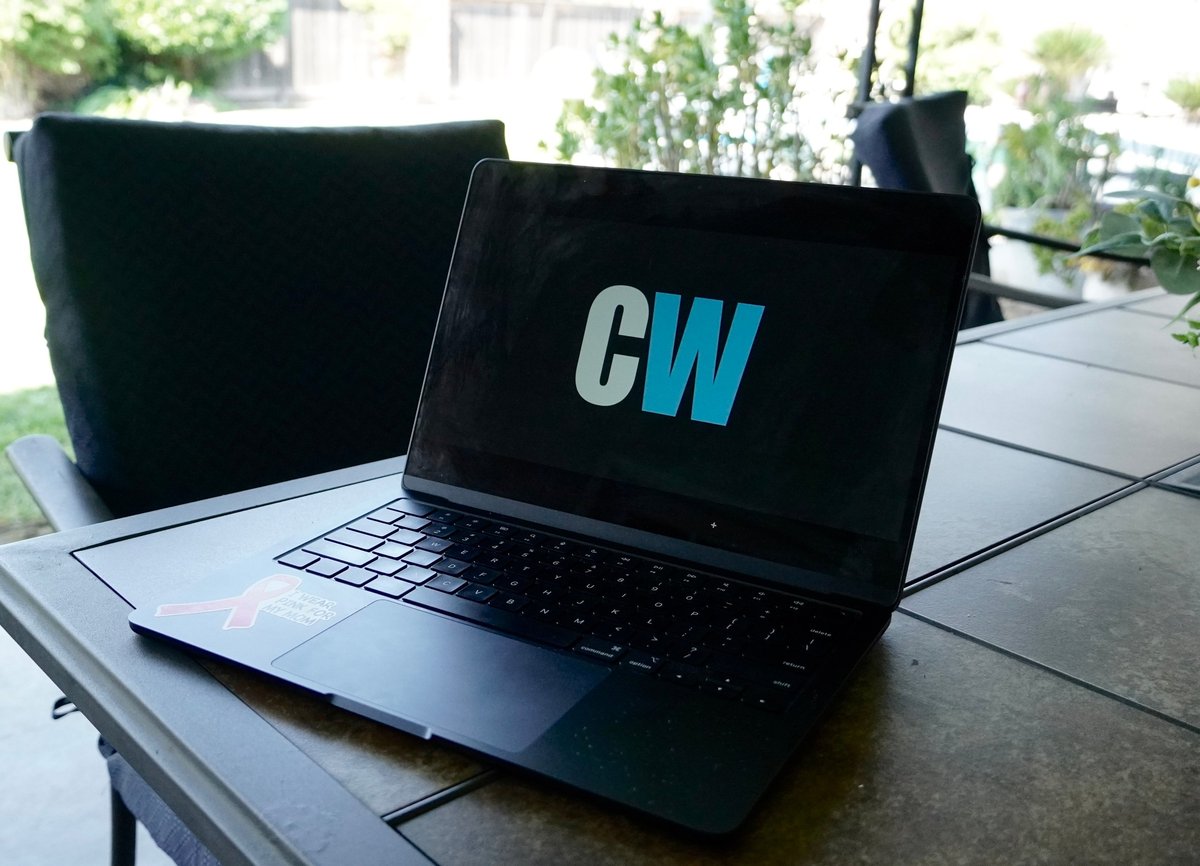 Two laptops on an outdoor table, with one displaying a blue CW logo on its screen
